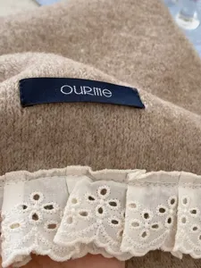 Close-up of knitted scarf detail featuring delicate white lace trim and brand label.