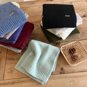 Detailed view of cozy knit winter scarves in multiple colors, featuring metal tag accents on table.