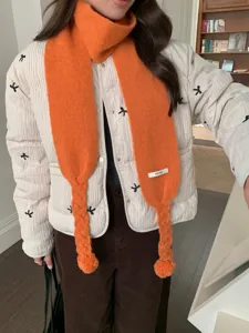 Close-up detail of cozy orange knitted scarf featuring stylish braided design and cute pom-poms.