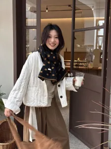 Detail view of a cozy black and brown polka dot wool scarf worn by a model in a cafe setting.