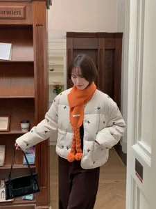 Cozy orange knitted pom-pom scarf styled with quilted winter jacket in lifestyle detail view.