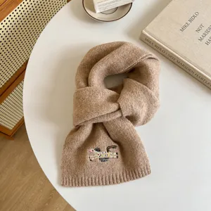 Detailed view of brown knitted wool blend scarf with cute embroidered pony design for winter.
