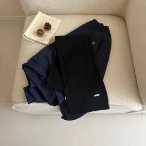 Detailed view of cozy dark blue sweatshirt and black knit scarf styled on white chair.