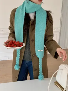 Chic teal knit scarf featuring playful braided tassels and fluffy pom-pom ends for cozy winter style.