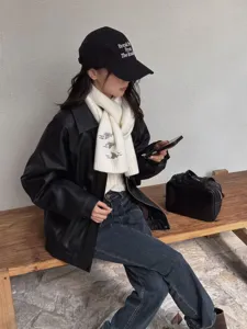Detail shot of women's knitted scarf featuring cute embroidery, paired with leather jacket and cap.