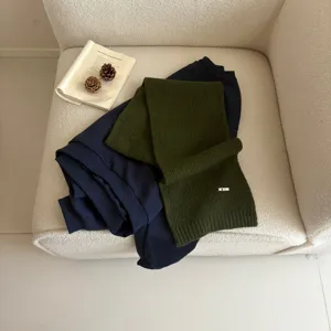 Detail view of dark green knit scarf and navy top styled on a cozy white armchair.