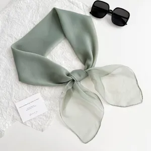 Detailansicht des salbeigrünen quadratischen Schals mit Sonnenbrille auf weißem Untergrund.