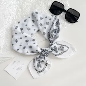 Detailed view of white square scarf with black paisley and floral patterns, elegant design.