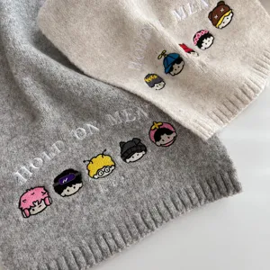 Close-up detail of knitted wool winter scarf with cute cartoon embroidery and English text.