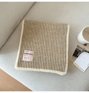 Close-up detail of knitted wool blend scarf in khaki tone, neatly folded on sofa.