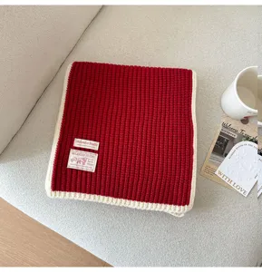 Close-up detail of cozy red knit scarf with white trim and brand tag, soft winter accessory.