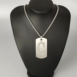 Detail shot of stainless steel dog tag necklace featuring a carved letter C pendant.
