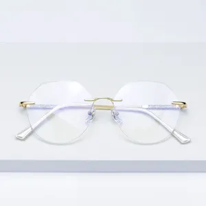 Detailopname van een frameloze zeshoekige bril met gouden metalen veren en glitteraccenten.