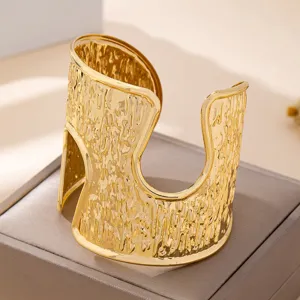 Primo piano del bracciale rigido largo in metallo dorato con finitura testurizzata.