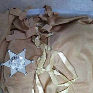 Western cowboy costume detail shot featuring ribbon lacing and a silver sheriff star badge.