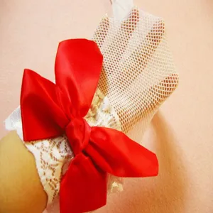 Close-up of white fishnet hosiery featuring delicate lace trim and a large red satin bow.