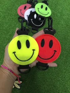 Kleurrijke smiley golfbal tasouder met zwarte karabijnhaak van zacht viltmateriaal.