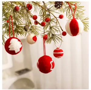 Nahaufnahme handgefertigter Weihnachtskugeln aus Filz an Tannenzweigen mit roten Beeren dekoriert.