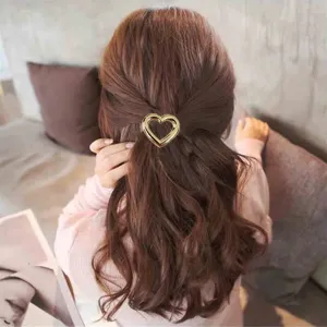 Dettaglio molletta per capelli a cuore dorata con texture metallica per look casual.