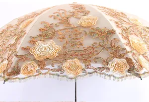 Close-up detail of luxurious beige lace umbrella with golden floral embroidery and fringe.