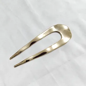 Primo piano dettagliato della forcina per capelli dorata minimalista a U con finitura metallica.