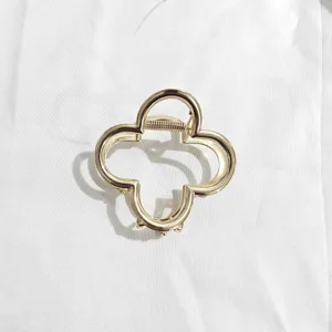 Gold four-leaf clover metal hair claw clip detail shot, elegant daily hair styling accessory.