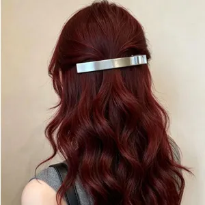 Close-up detail shot of minimalist silver metal hair barrette worn on wavy burgundy hair.