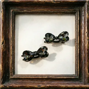 Close-up detail shot of exquisite black crystal heart hair clips set in a retro wooden frame.
