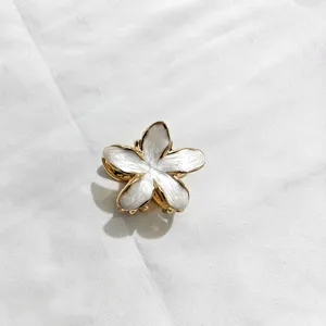 Dettaglio molletta per capelli a fiore di frangipani smaltato bianco con bordo oro.