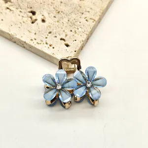 Detail close-up of mini blue crystal flower hair claw clip, elegant metallic side pin.