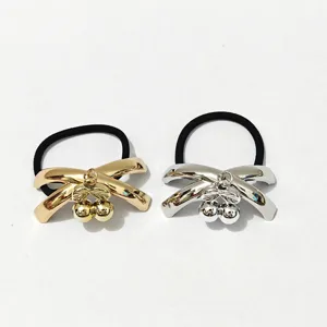 Detailed view of metal bow hair tie with cherry charm, glossy gold and silver finish.