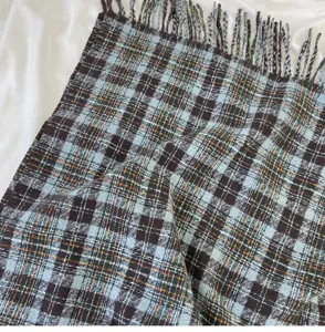 Detailed close-up of blue and brown plaid scarf texture with fringes on white background
