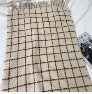 Close-up detail of the classic beige plaid scarf showing soft texture and neat tassel fringe.