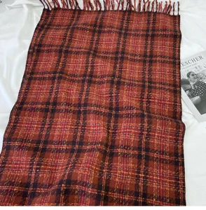 Detailed view of a cozy red and brown plaid scarf featuring elegant fringes and soft texture.