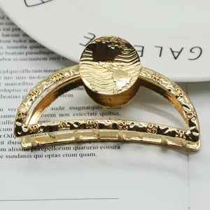 Gold metal hair claw clip with zodiac and globe pattern, minimalist geometric design detail.