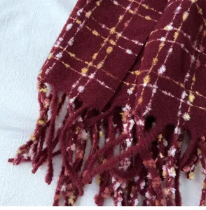 Detail shot of dark red plaid winter scarf showing soft textured fabric and elegant fringe ends.