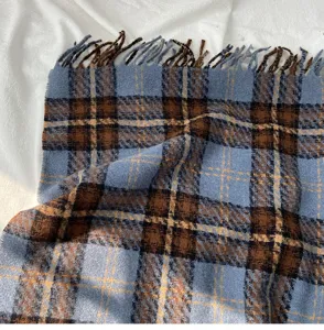 Close-up detail of soft winter plaid scarf with blue and brown pattern and fringe edges.