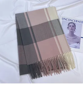 Close-up of a soft pink and grey plaid winter scarf with delicate tassel fringe details.