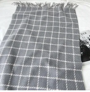 Close-up detail of grey plaid cashmere-feel scarf with fringe, soft winter accessory texture.