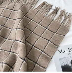 Detailed close-up of warm winter plaid scarf with fringe, soft cashmere-feel fabric texture.