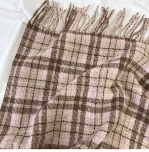 Close-up detail of cozy pink and brown plaid scarf featuring soft textured fabric and chic tassels.
