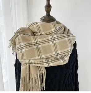 Close-up detail of the classic beige plaid winter scarf featuring soft fringe and warm texture.