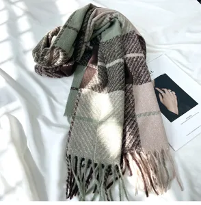 Close-up detail of cozy green and brown plaid scarf with stylish tassels on white fabric.