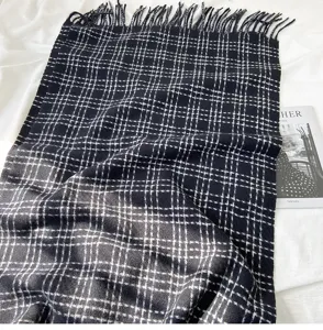 Vue détaillée de l'écharpe à carreaux noire et blanche avec des franges douces et un tissu.