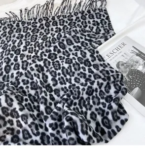 Detailed view of black and white leopard print scarf with cozy tassel trim texture close up.