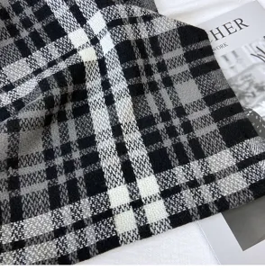 Close-up detail of soft black, white and grey plaid winter scarf texture showing cozy cashmere feel.