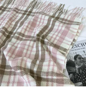 Close-up view of soft pink and brown plaid winter scarf featuring delicate fringe details.