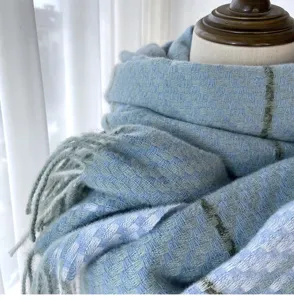 Close-up detail of soft blue and green plaid winter scarf with fringed hem texture display.