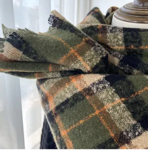 Detailed view of cozy green and orange plaid winter scarf with chic fringe hem texture.