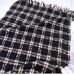 Detail view of a cozy black, white and brown plaid winter scarf with chic fringe edges.